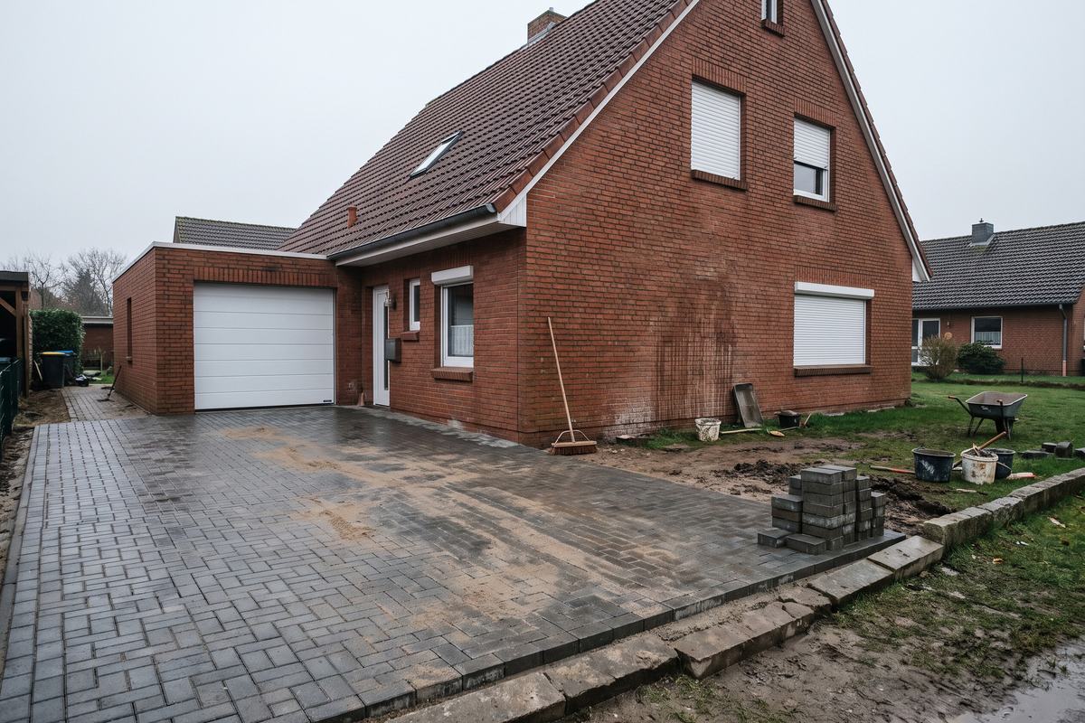 Fertig gepflasterte Einfahrt mit grauen Betonsteinen und Bordsteinkante vor einem Backsteinhaus